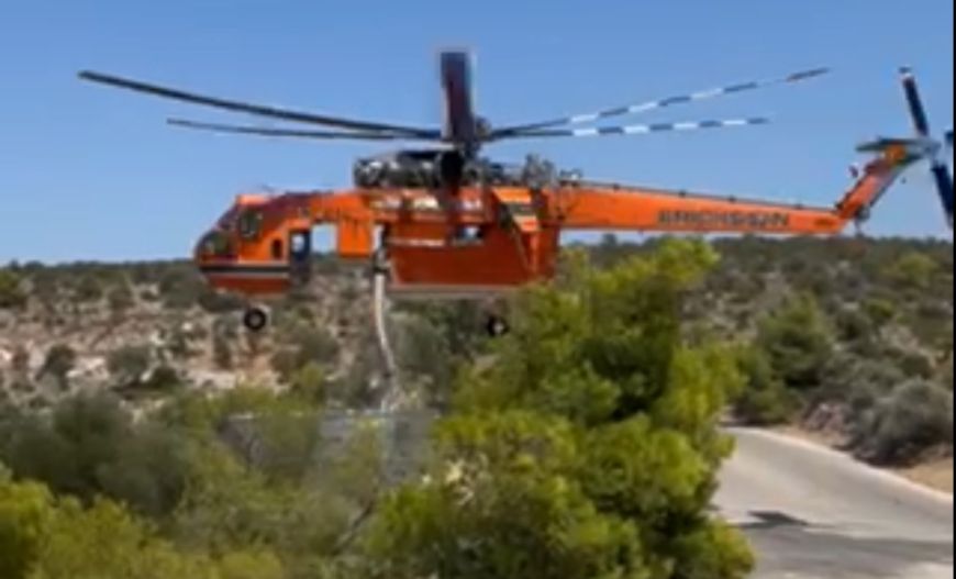 Firefighting helicopter scooping water from an ASKOMET tank to extinguish the fire in Koropi, Attica.